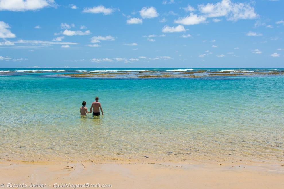 Imagem de duas pessoas com águas claras pela cintura na Praia Taipu de Fora.